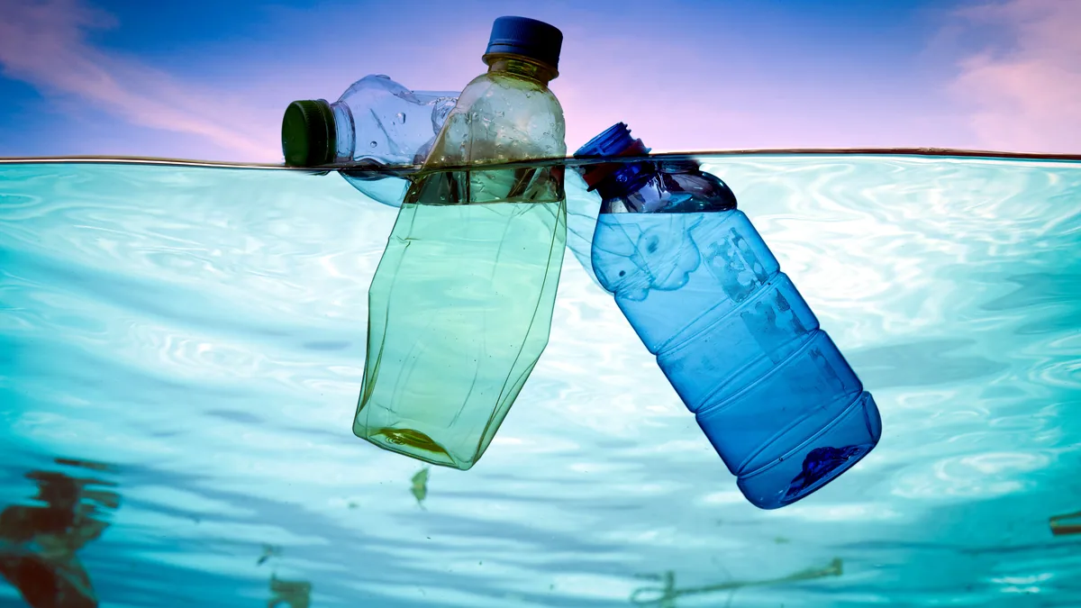 Botellas plasticas flotando en el agua turquesa cerca de una playa desierta.