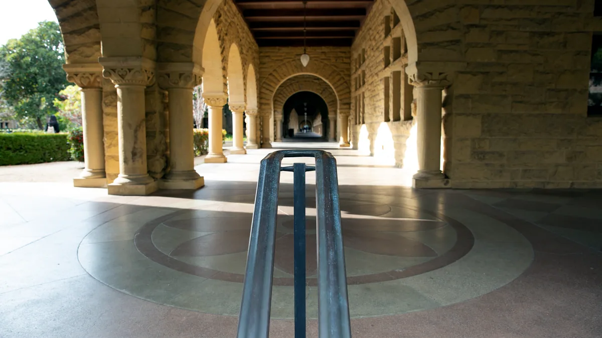 Un patio interior con columnas de piedra y estudiantes caminando al sol.