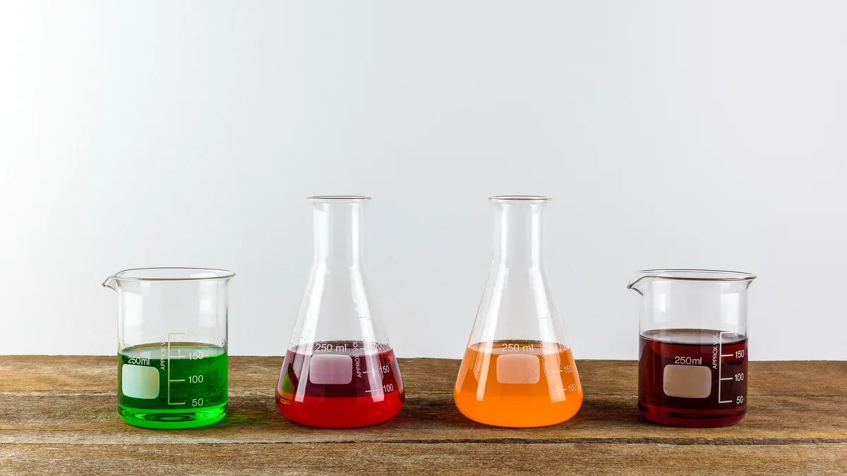 Varios matrazes de vidrio con liquidos de distintos colores sobre una mesa.