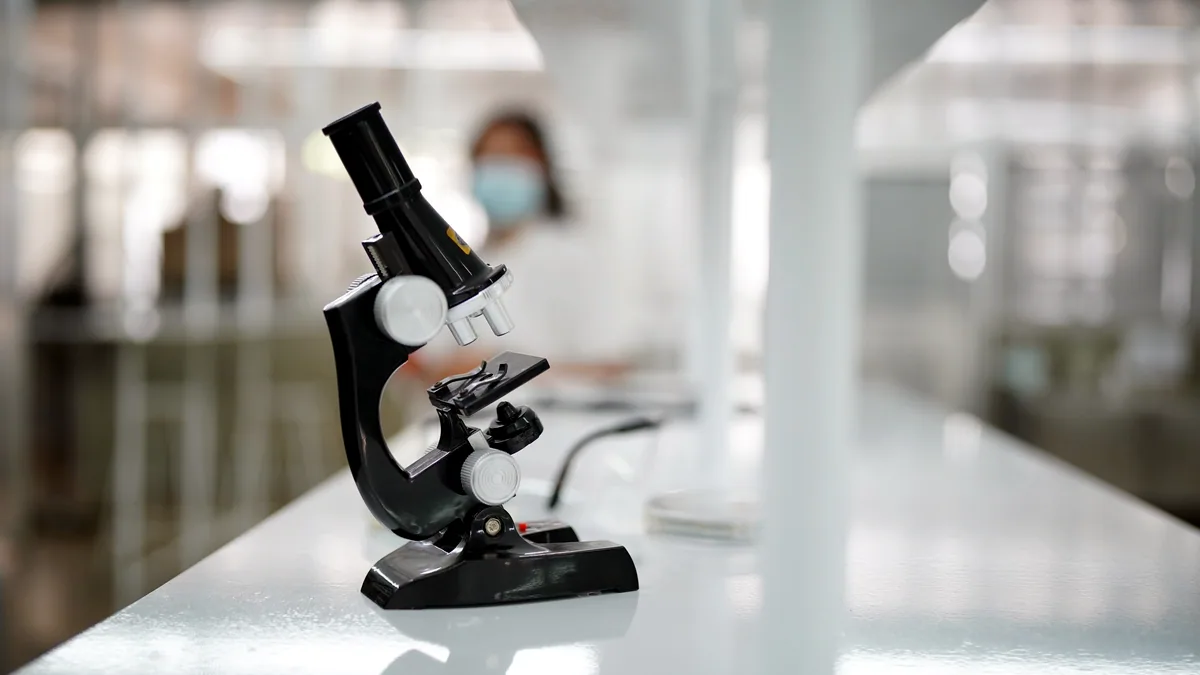 Un microscopio de laboratorio sobre una mesa de trabajo iluminada por luz natural.