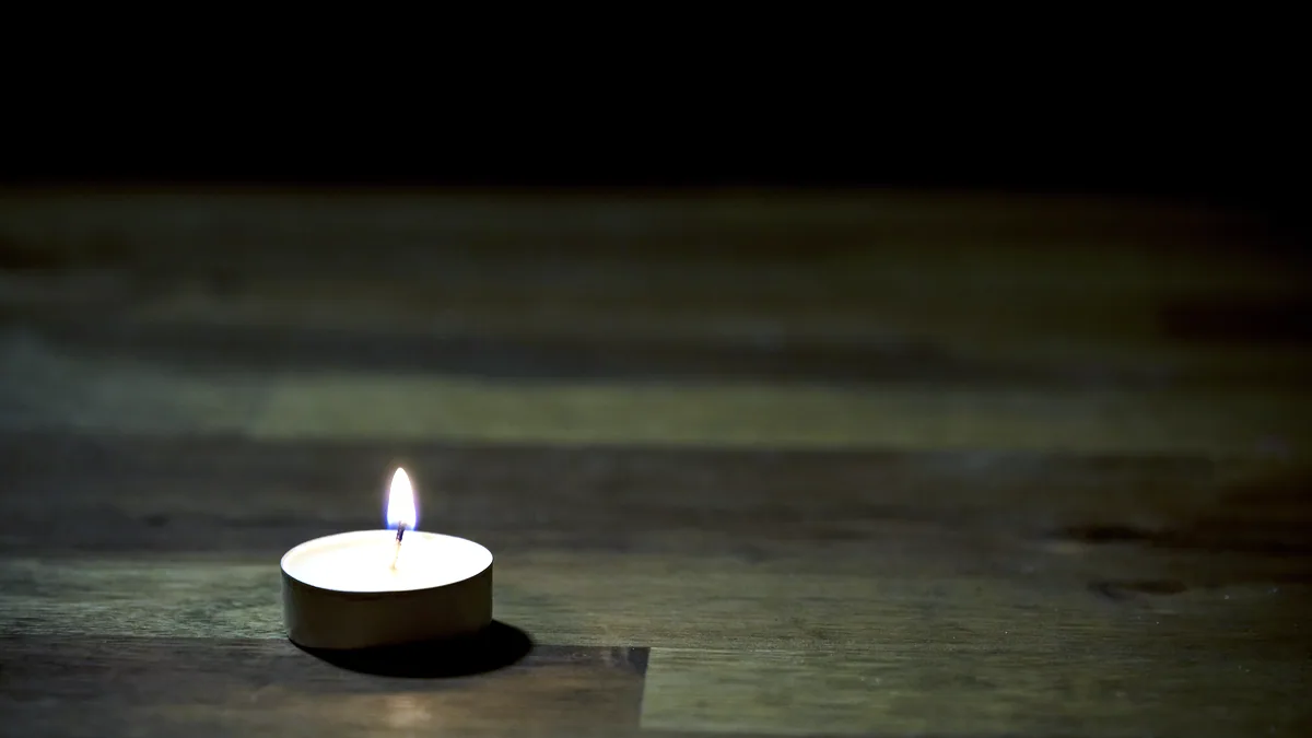 La llama de una vela encendida sobre una mesa oscura con sombras suaves a los lados.